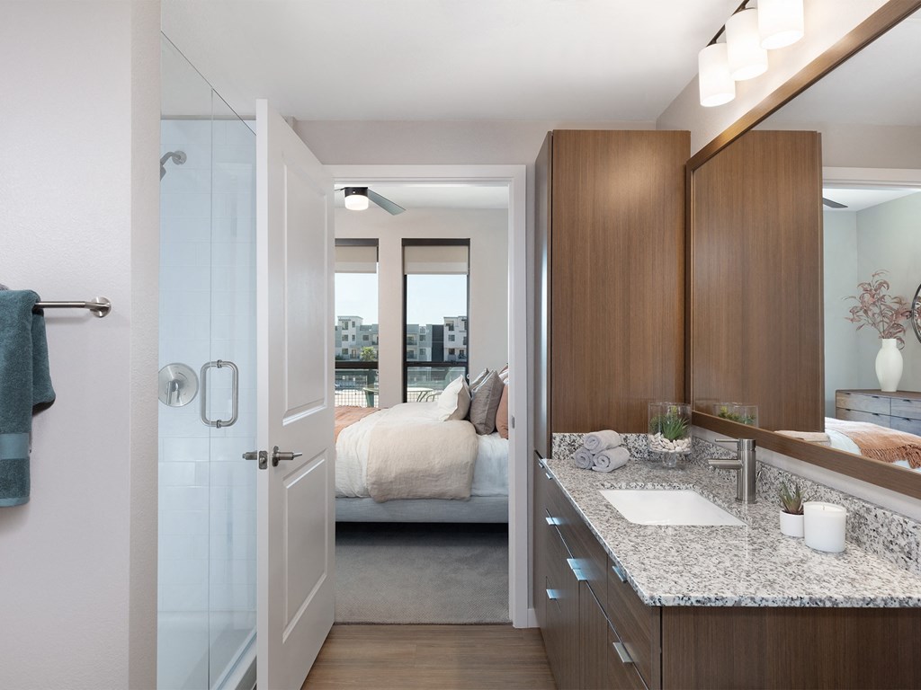 a bathroom with a sink and a mirror and a bedroom in the background
