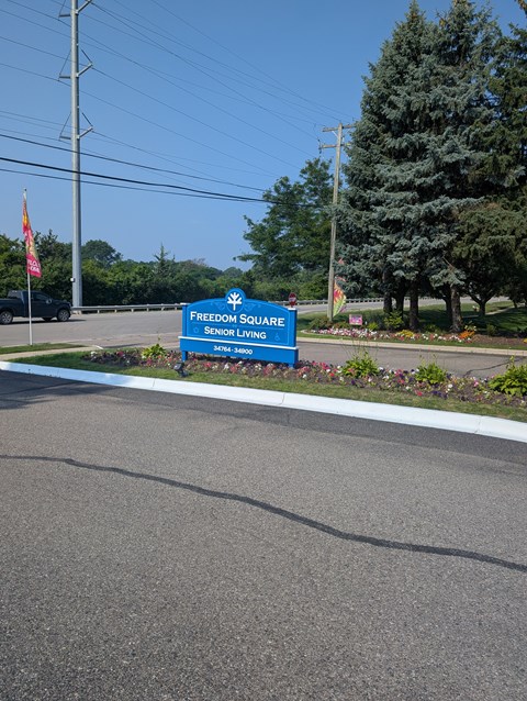 A sign for Freedom Square Senior Living stands in front of a tree.