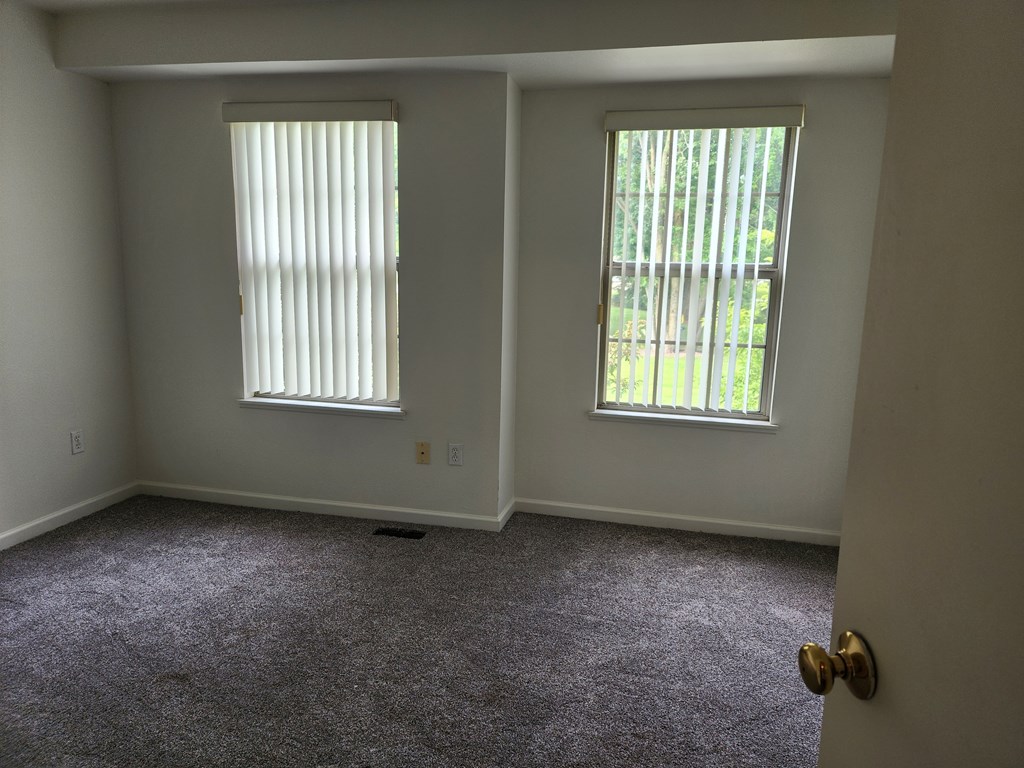 A room with two windows and carpeted floor.