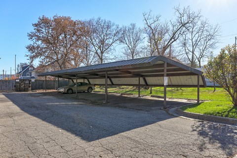 A carport with a car inside is situated in a parking lot.