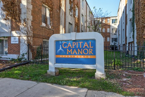 A sign for Capital Manor Apartments is in front of a brick building.