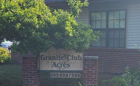 A sign for Granite Club Acres stands in front of a house.