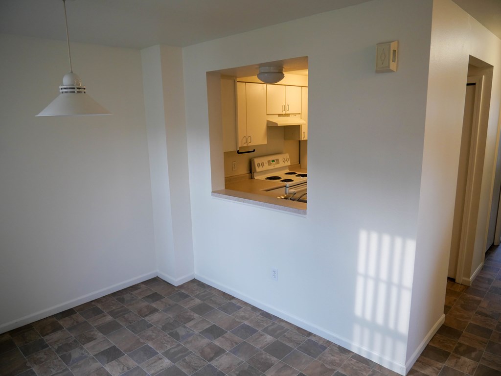 A kitchen is visible through a window in a white room.