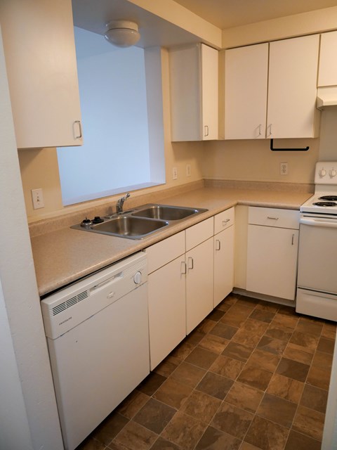 A kitchen with white cabinets and brown tiles.