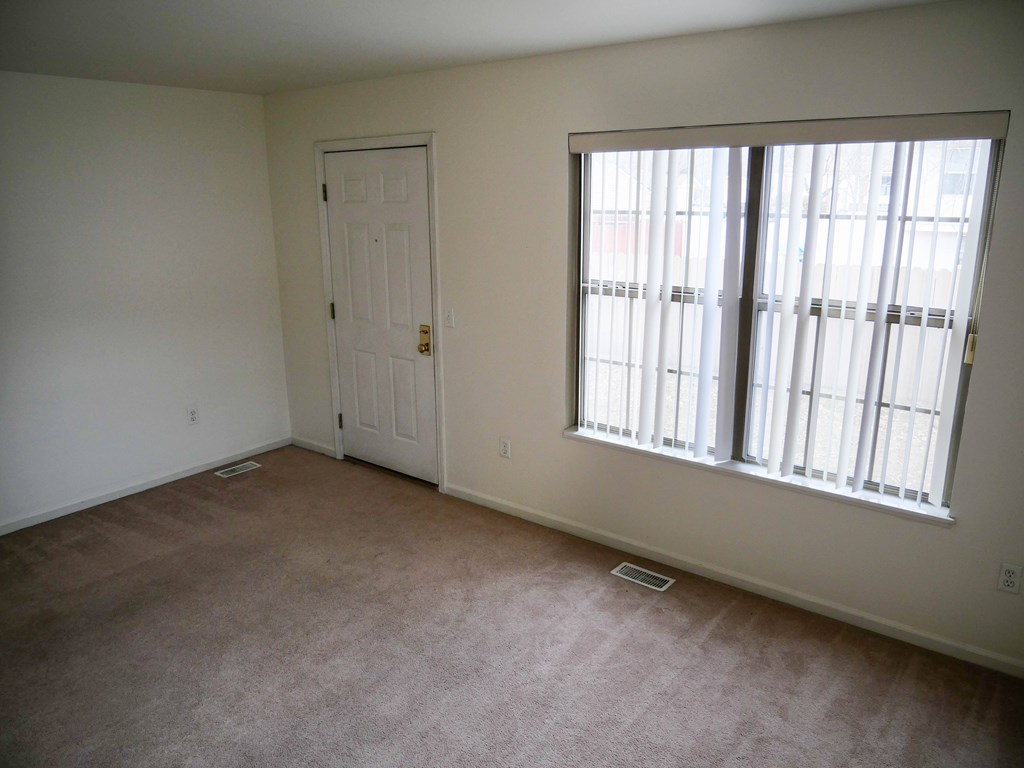 A room with a carpeted floor, a door, and a window with blinds.