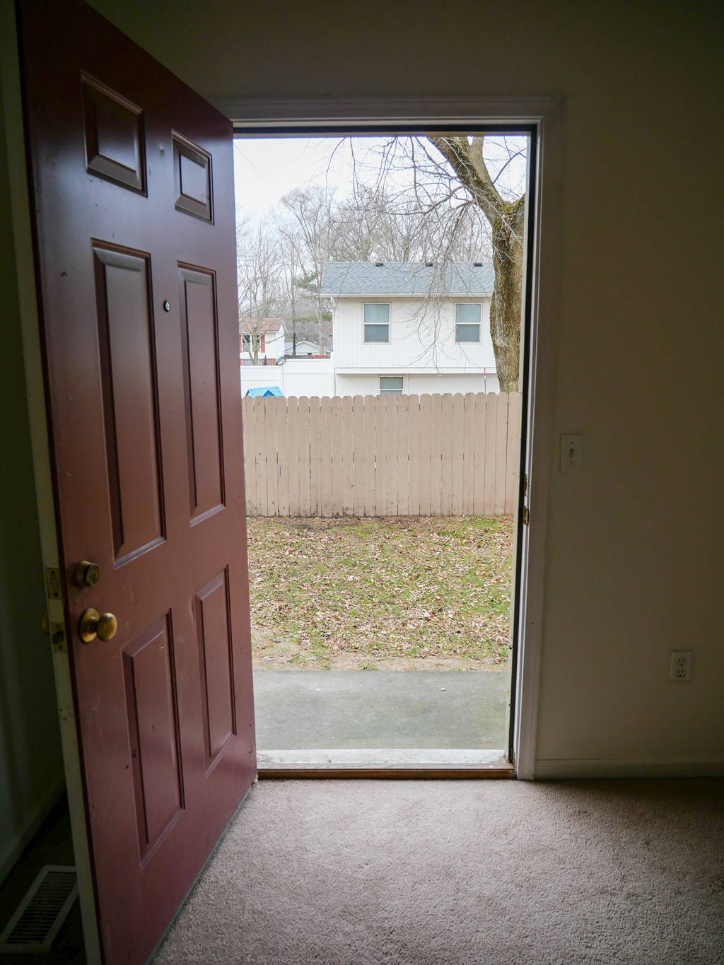 A red door is open to a backyard.
