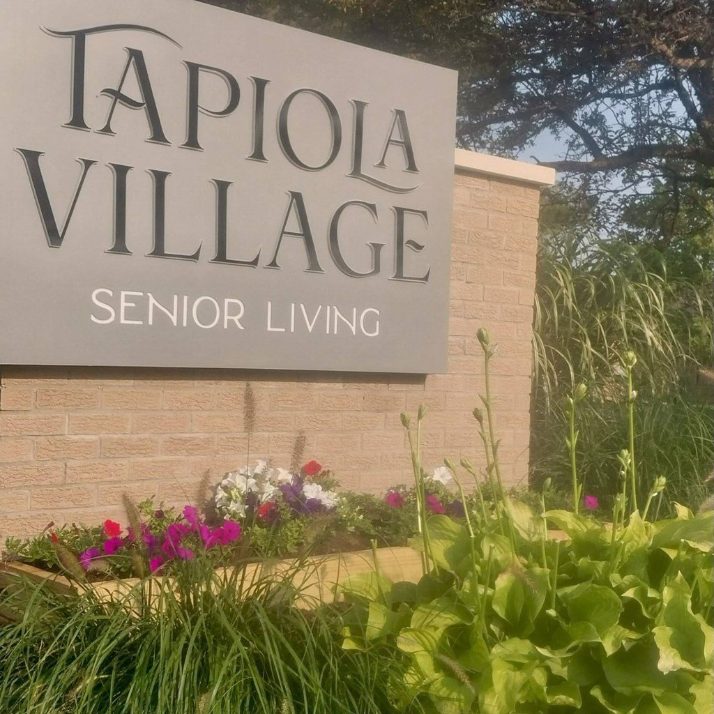 A sign for Tapiola Village Senior Living is displayed in front of some plants.