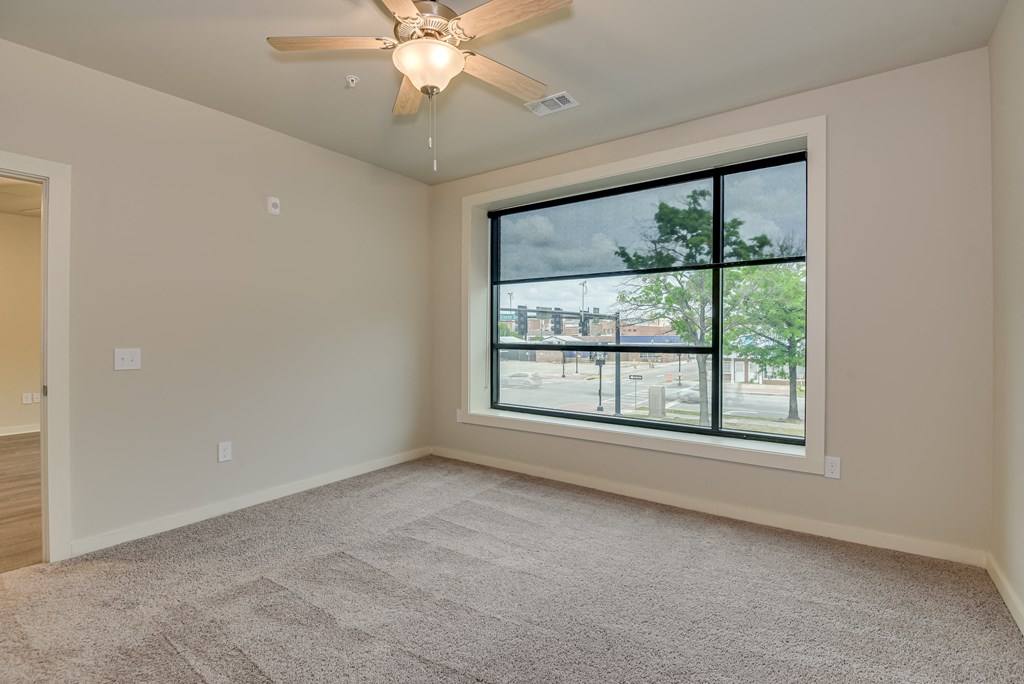 an empty living room with a large window and a ceiling fan