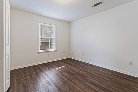 A room with wooden floors and a window with blinds.