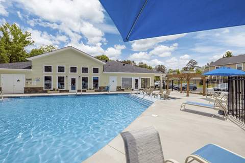 A large swimming pool with a blue umbrella and chairs around it.