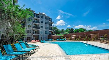 A swimming pool surrounded by blue lounge chairs and apartment buildings at The Collective NoDa, Charlotte