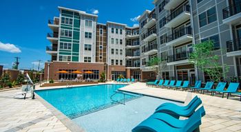 A large swimming pool with blue lounge chairs in front of apartment buildings at The Collective NoDa, Charlotte
