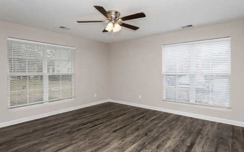 an empty living room with a ceiling fan and two windows