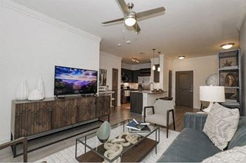 A modern living room with a flat screen TV and a ceiling fan at Cue Luxury Apartments, Cypress, Texas