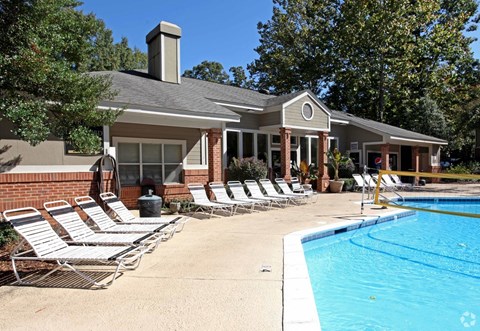 A poolside scene with a house and lounge chairs.