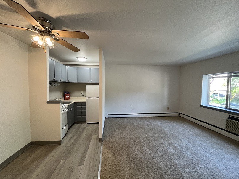 an empty living room with a ceiling fan and a kitchen