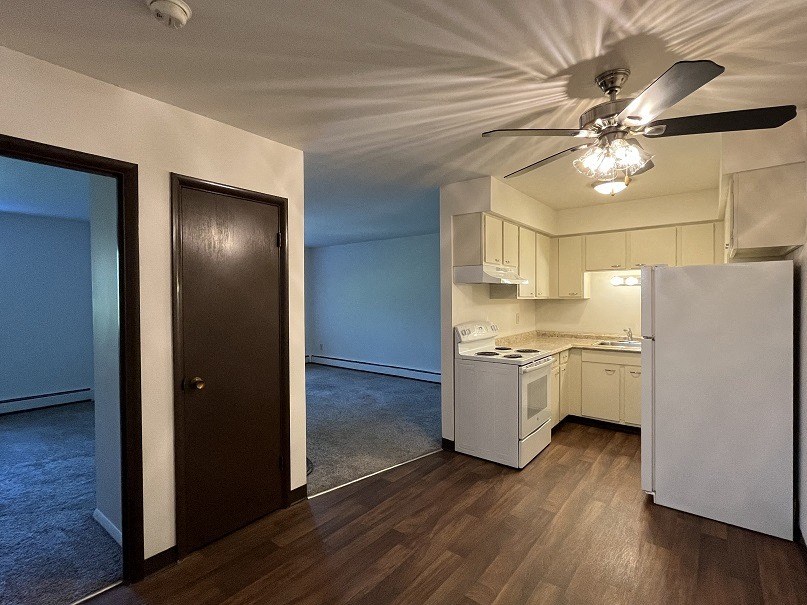 an empty living room with a ceiling fan and a kitchen
