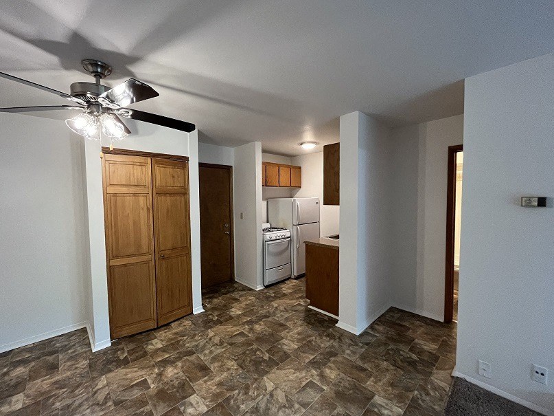 an empty living room with a ceiling fan and a kitchen
