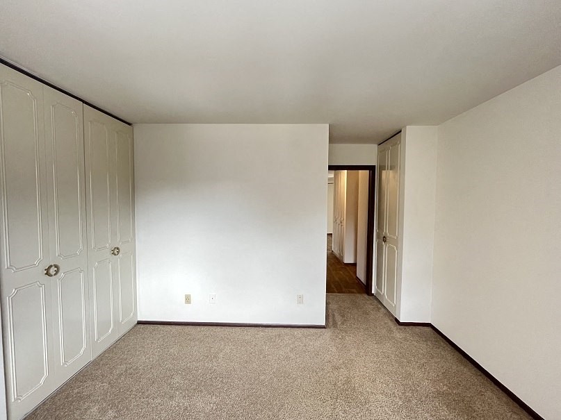 an empty bedroom with white closets and a carpeted floor
