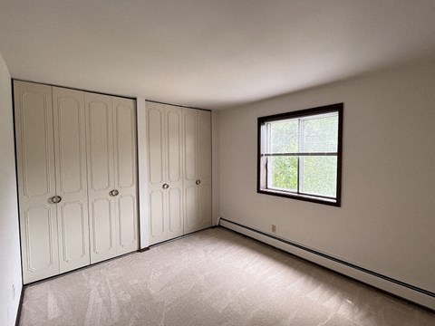 an empty bedroom with white cabinets and a window