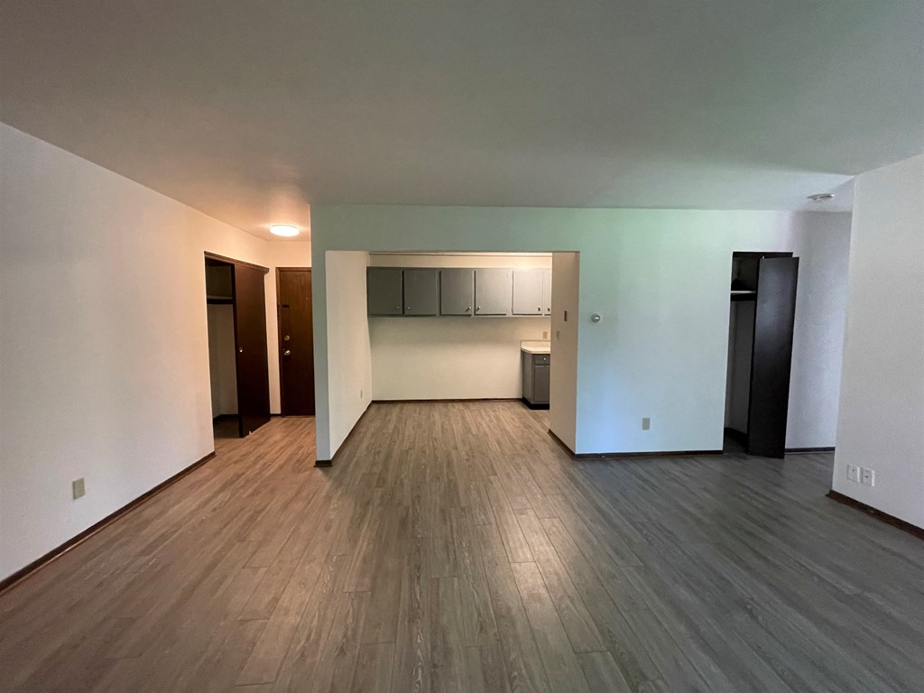 an empty living room and kitchen with wood floors and white walls