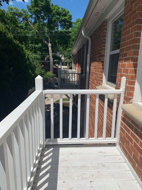 a small porch with a white railing and a brick building