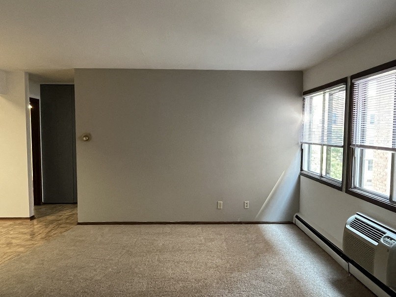 A room with a carpeted floor, a door, and a window with blinds.