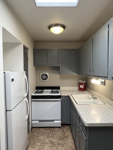 A kitchen with a white refrigerator, a white sink, and a black stove top oven.