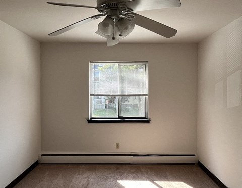 A room with a ceiling fan and a window with blinds.