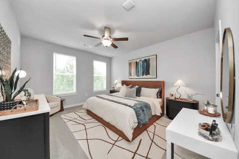 A bedroom with a king sized bed, night stand, dresser and a ceiling fan.