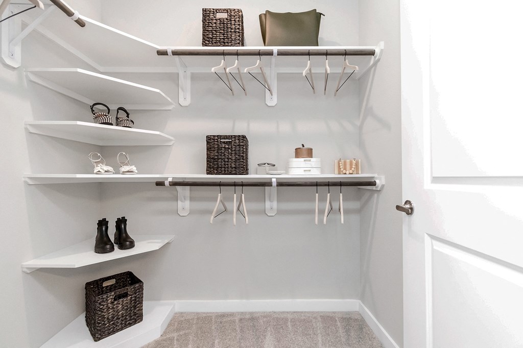 a walk in closet with white shelves and hooks and a white closet door with shoes