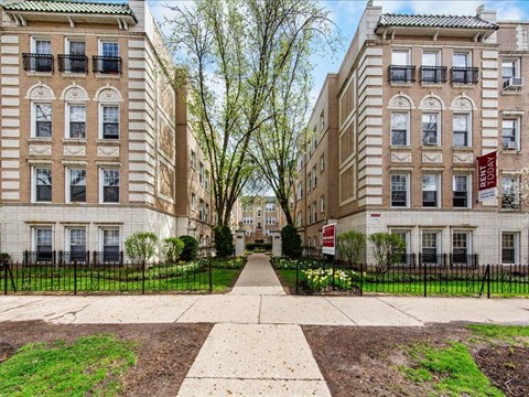 A row of brown and beige apartment buildings with green lawns in front.