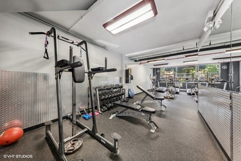 Fitness center at Presidential Apartments with benches, dumbbells, cardio machines and large window.
