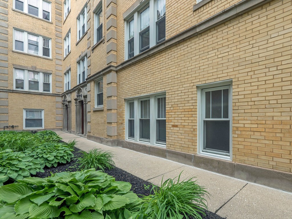a brick apartment building with a sidewalk and plants in front of it