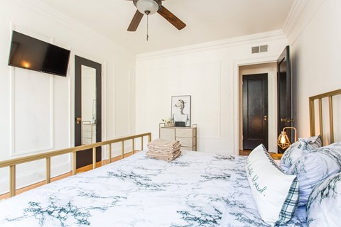 Bright bedroom with marble-print bedding, gold bedframe, dresser and TV at The Chatelaine Apartments in Gold Coast Chicago.