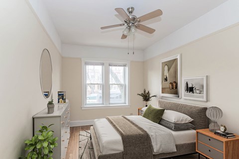 Bright bedroom with queen bed, dresser, ceiling fan, and window at Ashland Manor, Apartments in Ravenswood Chicago.