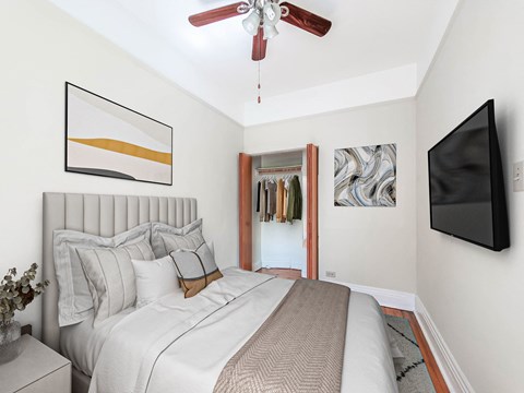 Bedroom at The Pehlam apartments in Lincoln Park Chicago with bed, wall-mounted TV, ceiling fan and open closet.
