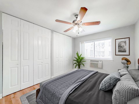 Bedroom at Grace Shores Apartments in Lakeview Chicago with large closet, ceiling fan, window AC, bed and plant.