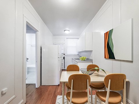 Dining area and galley kitchen with four orange chairs and white cabinets in Lakeview Chicago apartments.