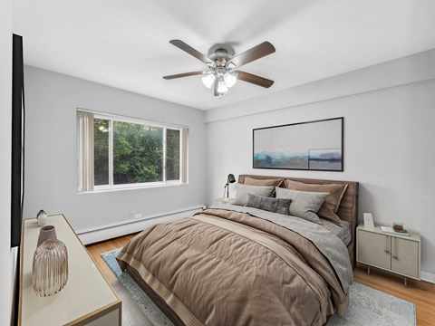 Bedroom with queen bed, ceiling fan, large window and neutral decor at Melrose Shores Apartments in Lakeview Chicago.
