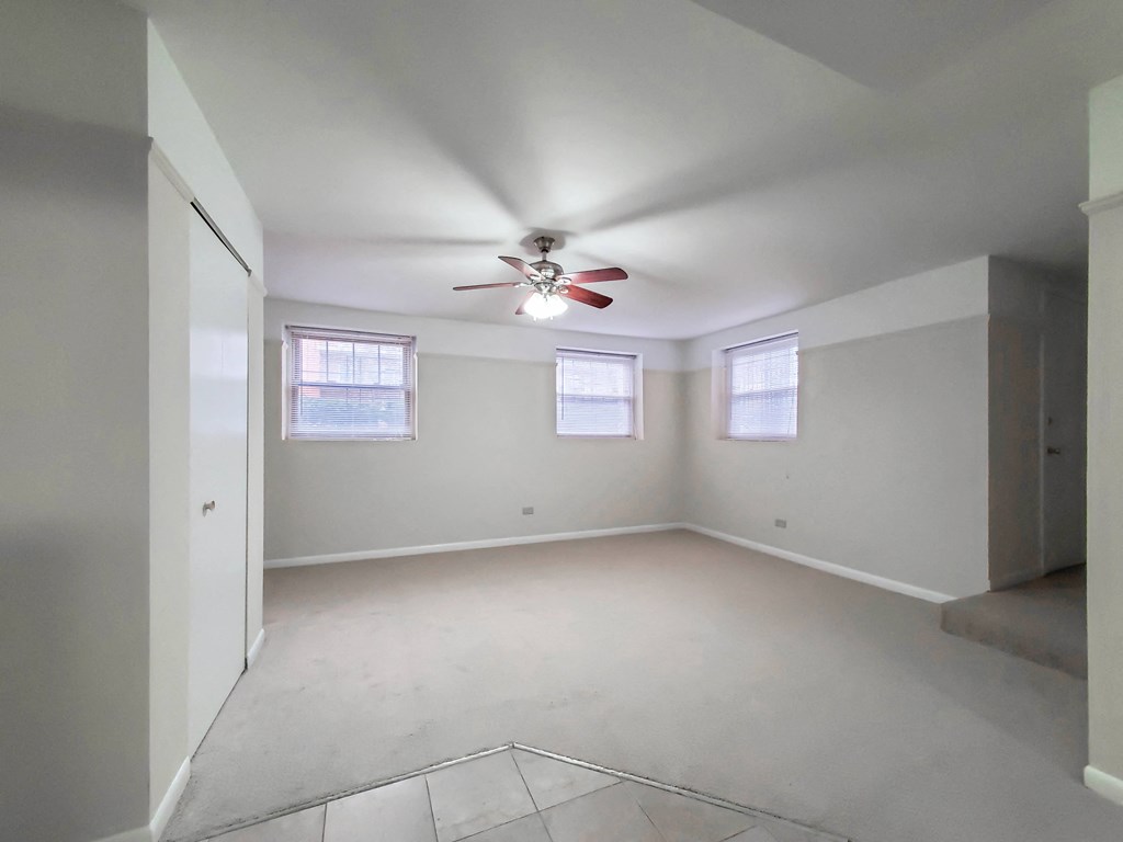 an empty room with a ceiling fan and three windows