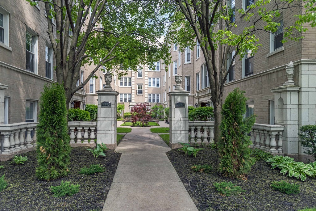 a walkway with trees and shrubs in front of an apartment building