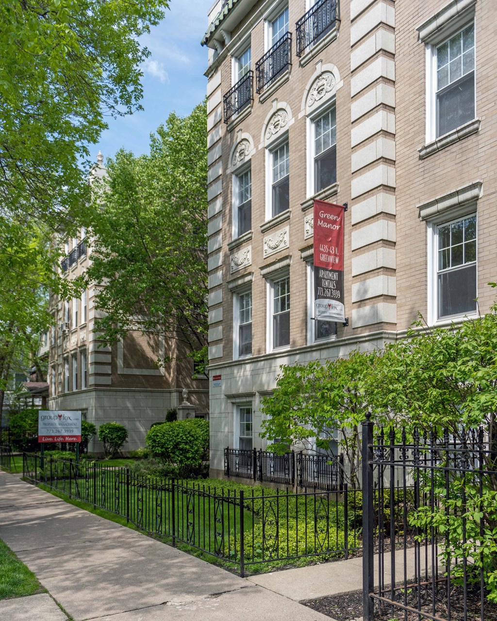 an apartment building with a black iron fence and a red sign on the side of the building