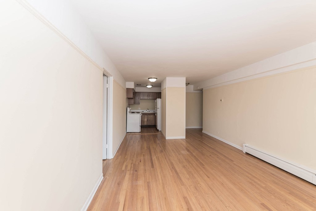 a bedroom with a hardwood floor and a kitchen in the background
