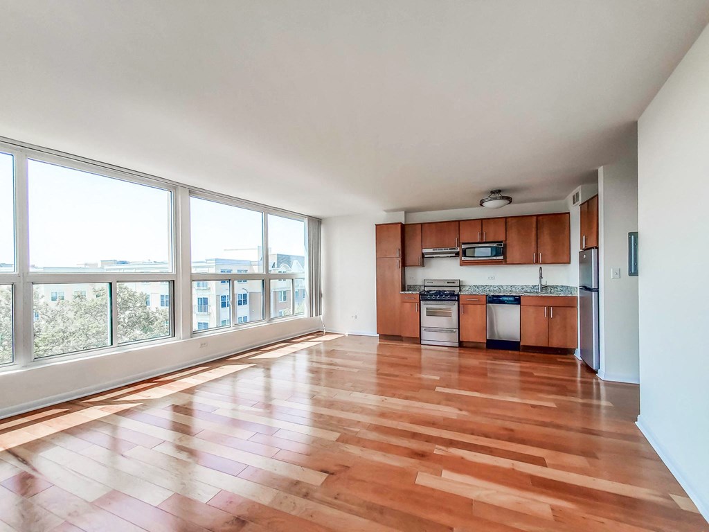 an empty living room and kitchen with wood floors and large windows