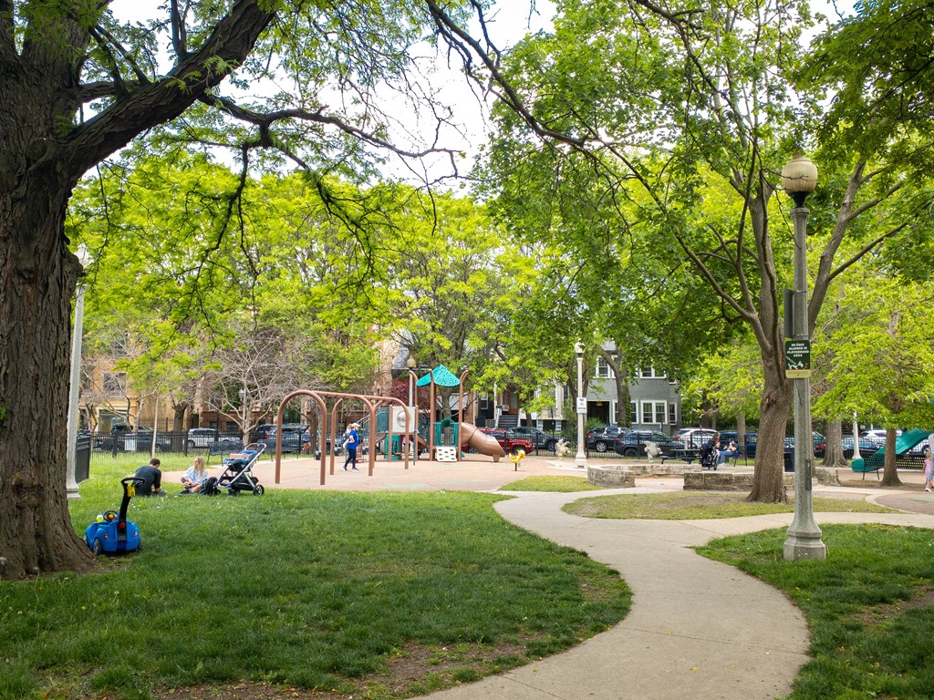 a park with green grass and trees and a playground in the background