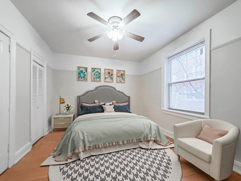 Furnished bedroom features bed, nightstand, ceiling fan, window, armchair, Park Shores Apartments in Buena Park Chicago.