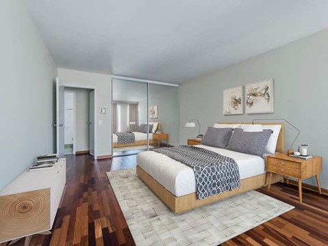 Bedroom with wood platform bed, mirrored closet, hardwood floors at The Van der Rohe, Apartments in Lakeview Chicago.