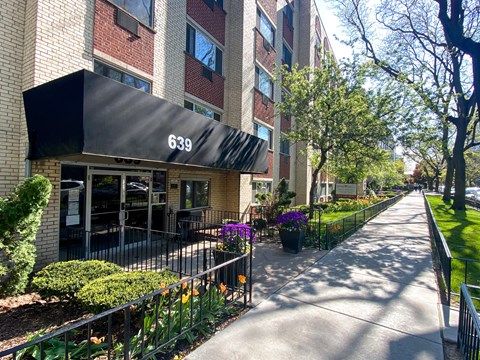 Grace Shores entrance at 639 with black awning, flower beds and tree-lined sidewalk, Apartments in Lakeview Chicago.