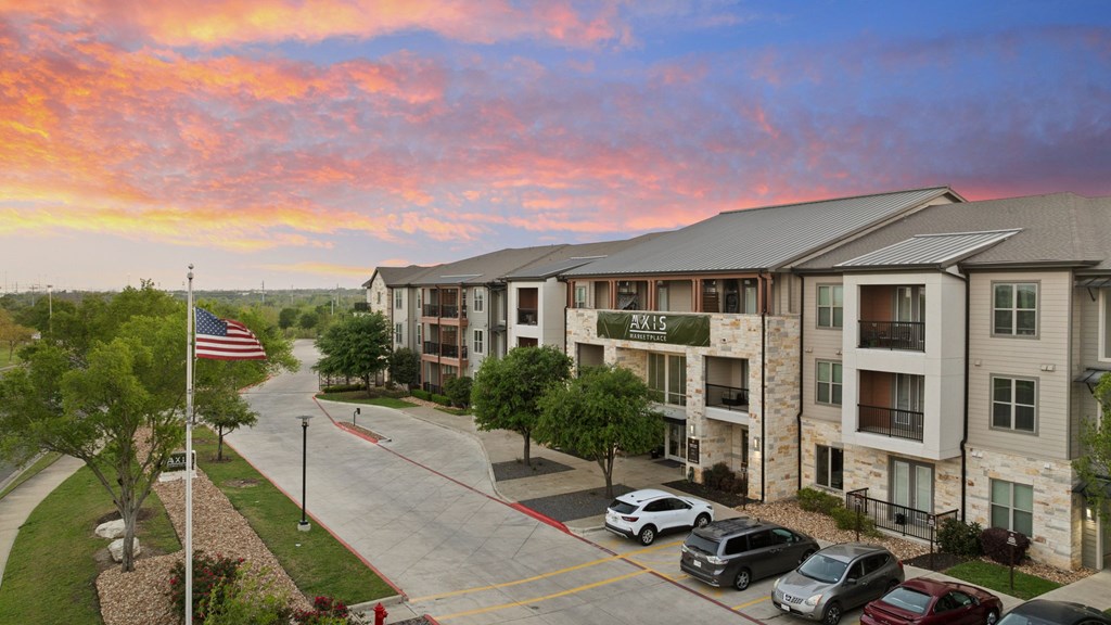A sunset view of apartment complex AX15 with cars parked in front.